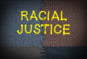 Brick Wall With "Racial Justice" Spray Painted In Yellow With A Crack Running Down The Middle